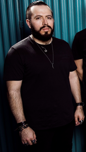 a picture of Diego Tejeida, the former keyboardist for the band Haken. he is wearing all black and standing awkwarldy with his bandmates